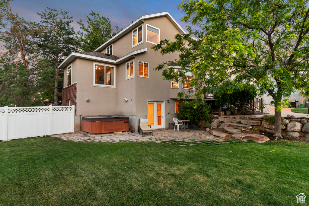 Rear view of property featuring a hot tub, stucco siding, a patio area, and stairs