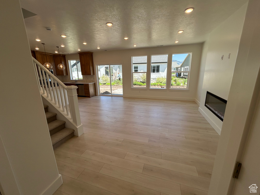 Unfurnished living room with recessed lighting, a glass covered fireplace, stairway, light wood finished floors, and a textured ceiling