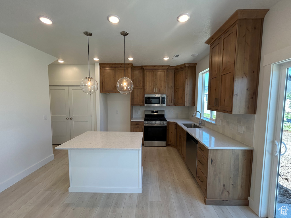 Kitchen with stainless steel appliances, light wood-style flooring, backsplash, brown cabinetry, and recessed lighting