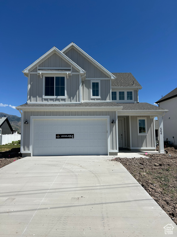 View of front of house with board and batten siding, a garage, concrete driveway, and roof with shingles