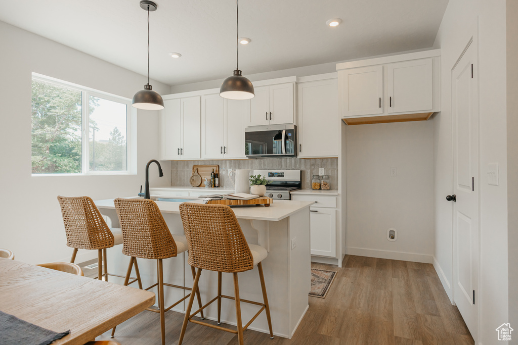 Kitchen with stainless steel microwave, gas range oven, light countertops, tasteful backsplash, and white cabinets
