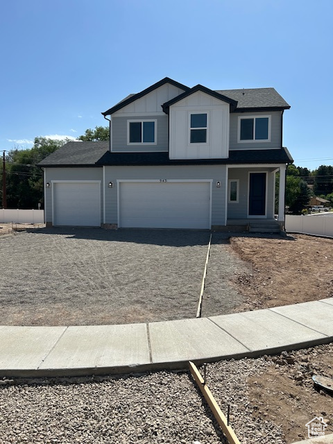View of front of house with an attached garage, driveway, board and batten siding, and roof with shingles