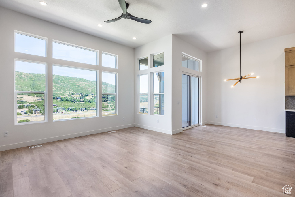 Unfurnished living room featuring a chandelier, recessed lighting, ceiling fan, light wood finished floors, and a mountain view