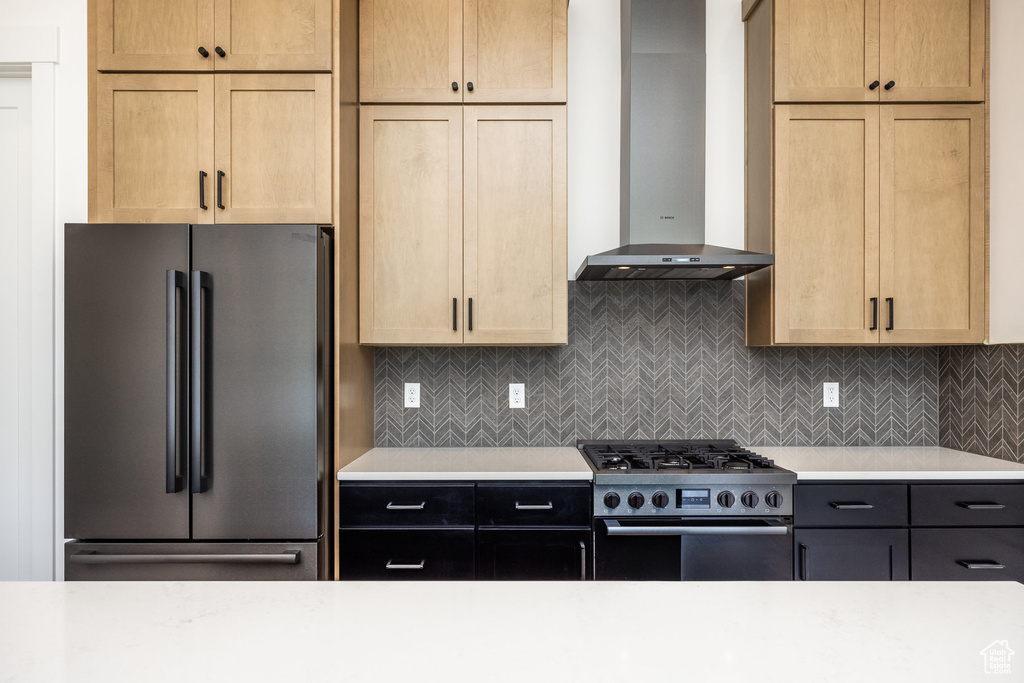 Kitchen featuring freestanding refrigerator, wall chimney exhaust hood, gas range, and light countertops