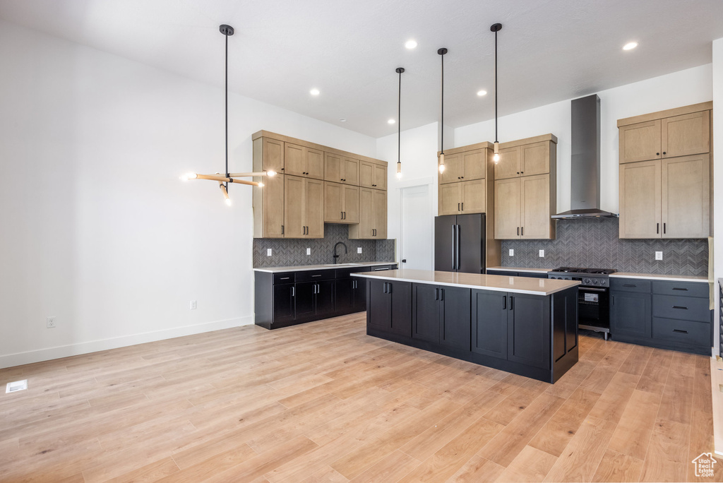 Kitchen featuring wall chimney exhaust hood, high end stove, freestanding refrigerator, light countertops, and a center island