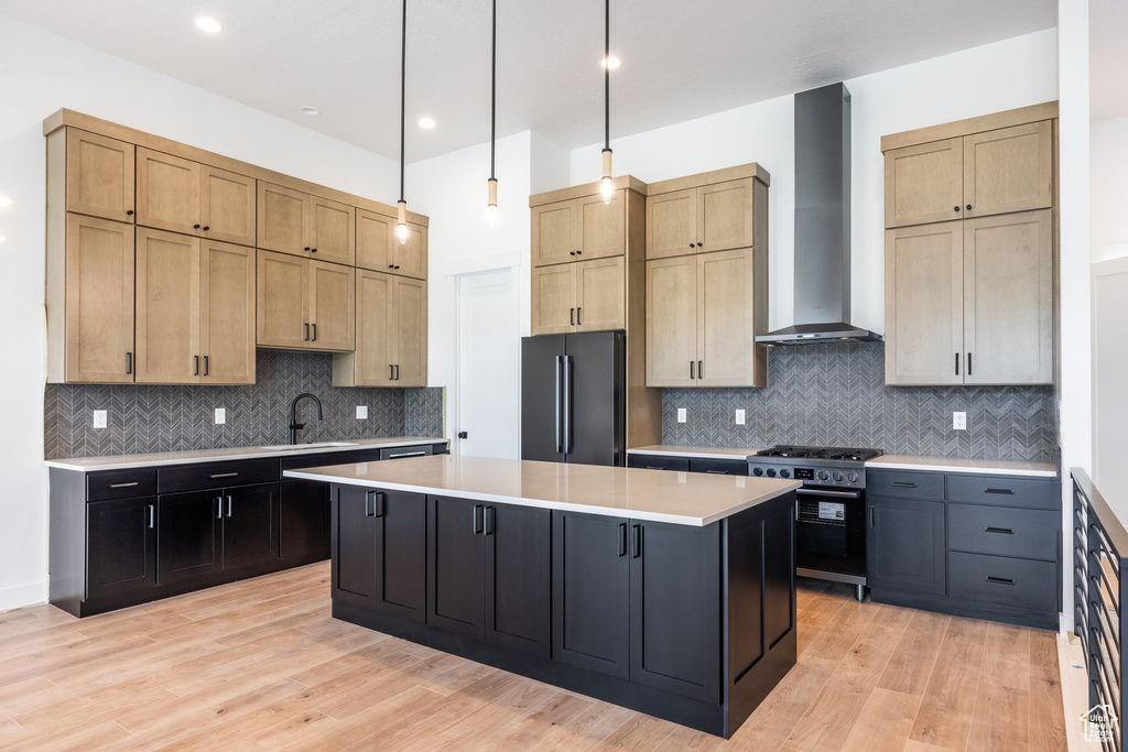 Kitchen featuring wall chimney exhaust hood, freestanding refrigerator, high end stove, a kitchen island, and light countertops