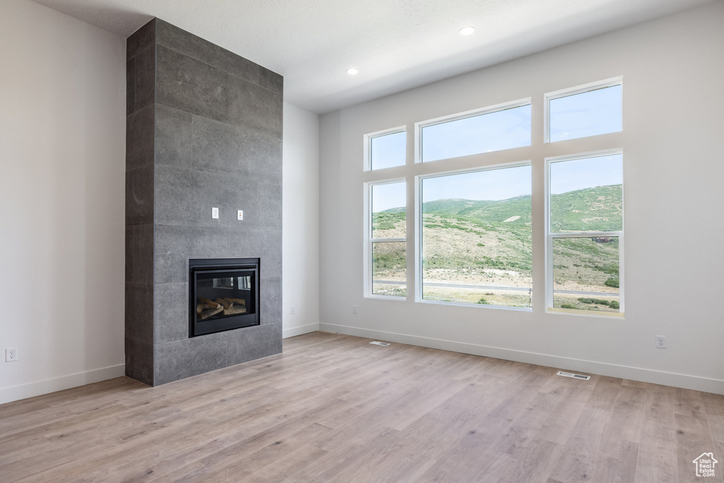 Unfurnished living room featuring a tiled fireplace, light wood-type flooring, and recessed lighting