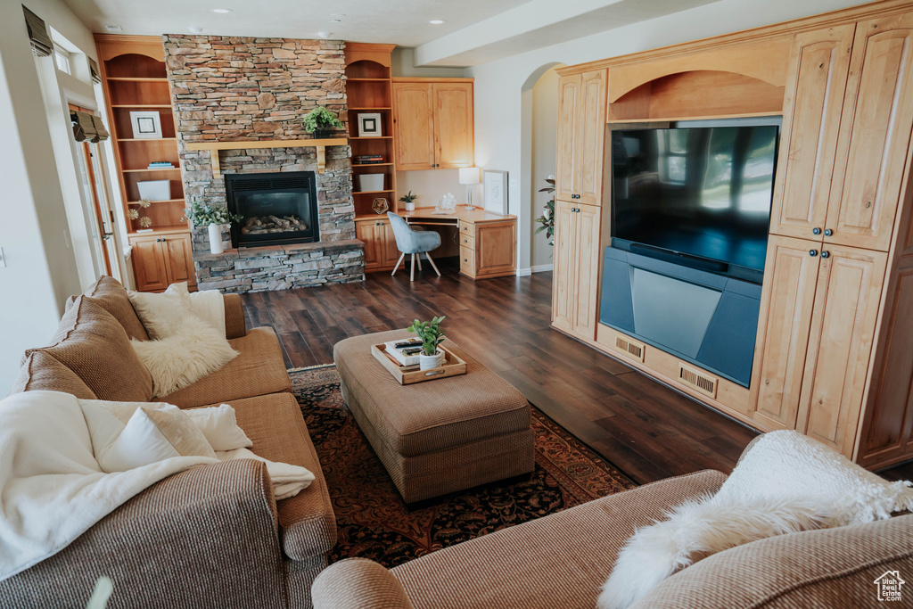 Living area with dark wood-style flooring, a stone fireplace, recessed lighting, arched walkways, and built in features