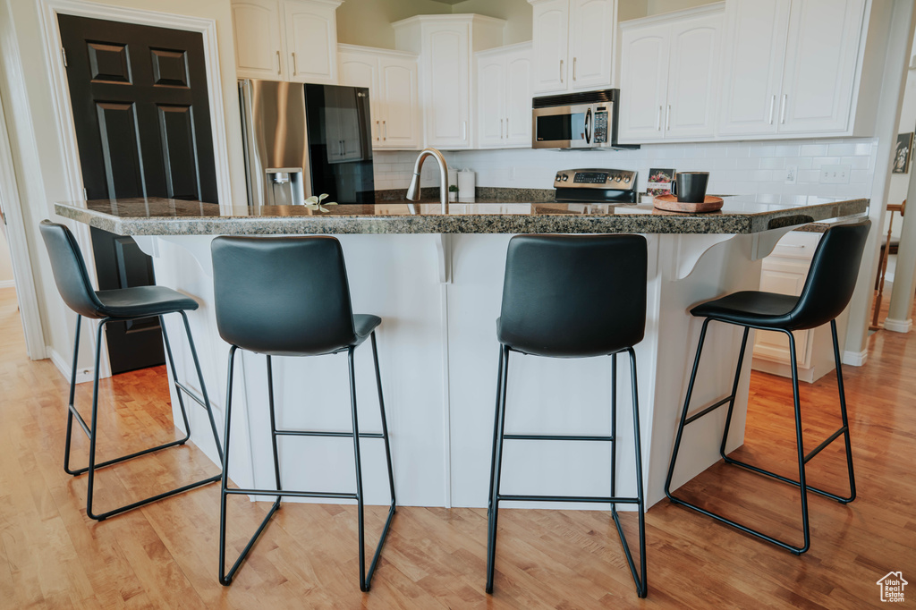 Kitchen featuring appliances with stainless steel finishes, a kitchen bar, white cabinetry, and light wood-style floors