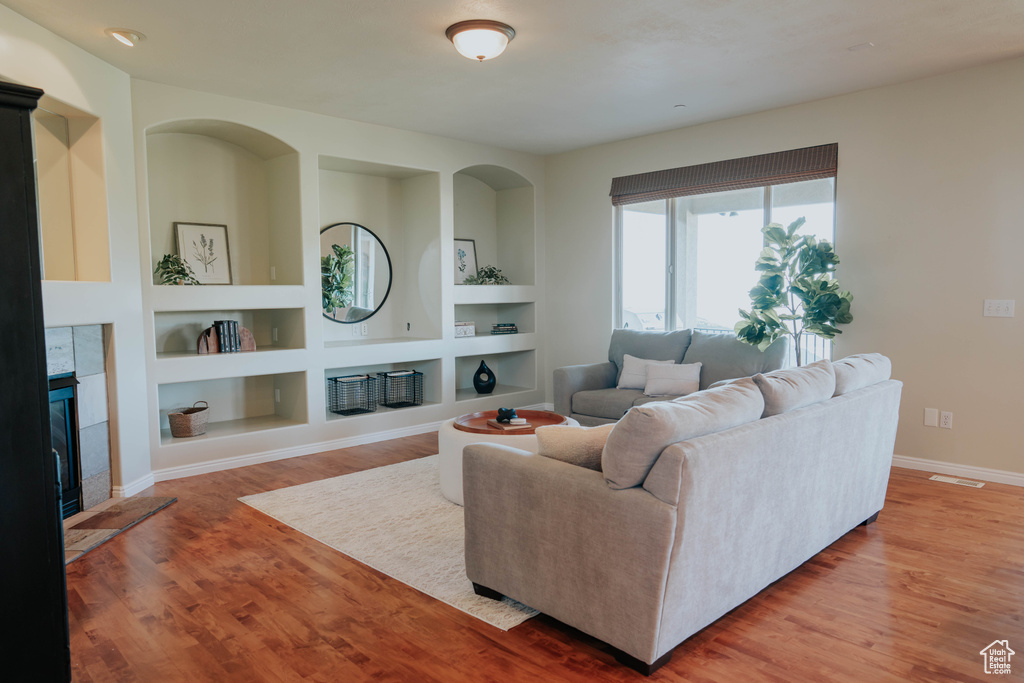 Living room featuring a tiled fireplace, wood finished floors, and built in shelves