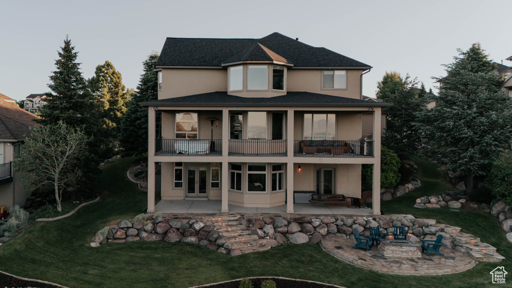 Back of house featuring a balcony, a patio, stucco siding, and a lawn