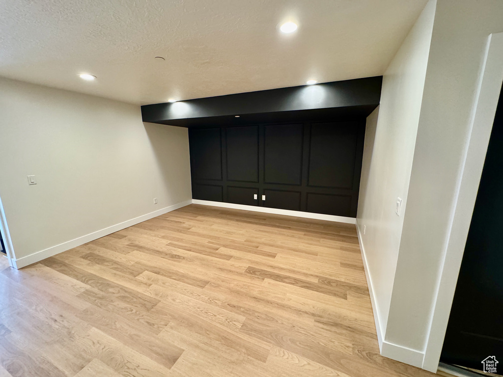 Finished basement with a decorative wall, light wood-style floors, a textured ceiling, and recessed lighting