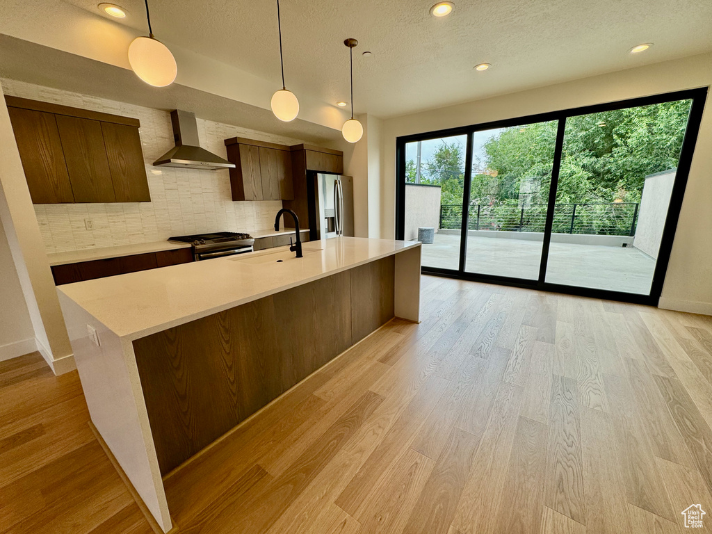 Kitchen featuring wall chimney range hood, appliances with stainless steel finishes, light countertops, modern cabinets, and a textured ceiling
