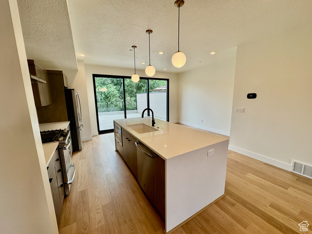 Kitchen featuring appliances with stainless steel finishes, light wood finished floors, light countertops, an island with sink, and a textured ceiling