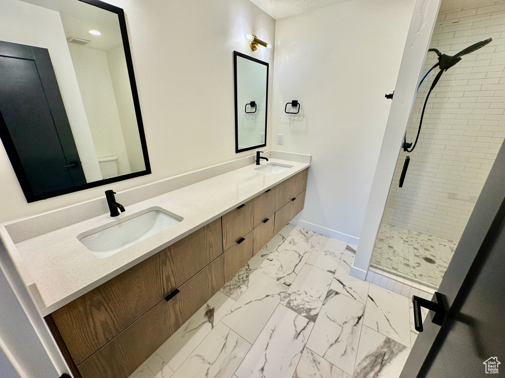 Bathroom featuring a shower stall, double vanity, marble finish floors, and recessed lighting