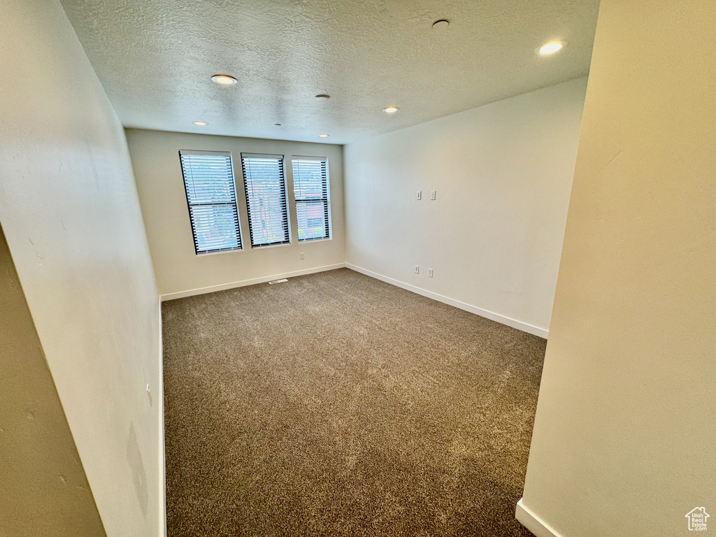 Unfurnished room featuring a textured ceiling, recessed lighting, and dark colored carpet