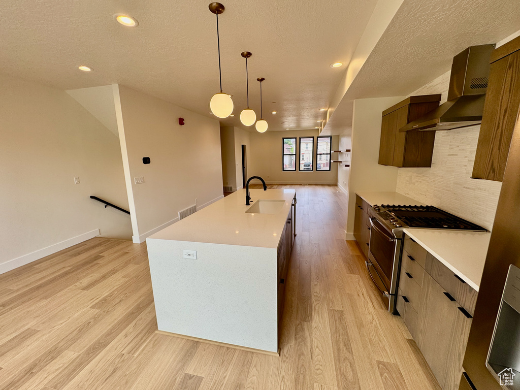 Kitchen with stainless steel gas range, wall chimney range hood, modern cabinets, light wood-style flooring, and recessed lighting