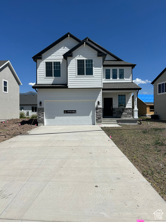 View of front of house with stone siding, a garage, concrete driveway, and a porch