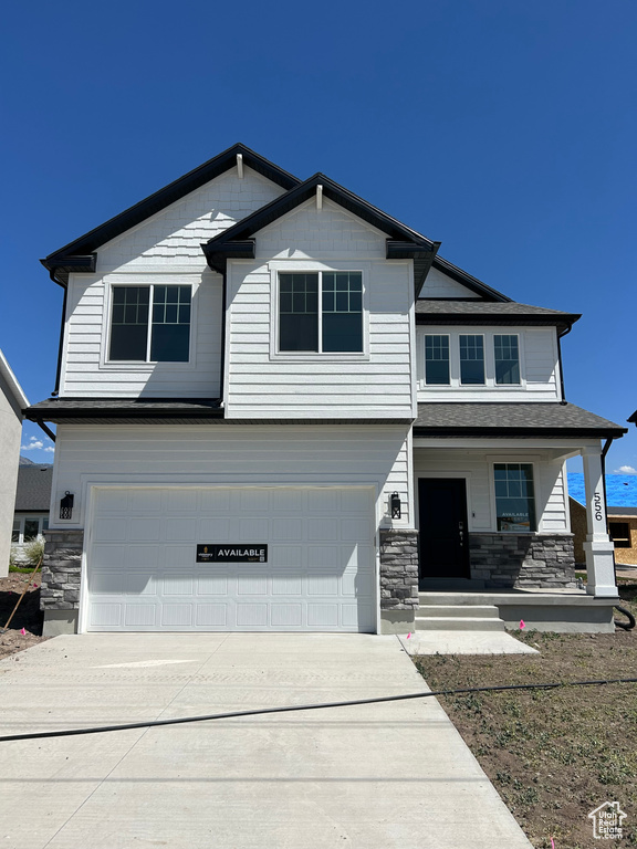 Craftsman inspired home with a garage, stone siding, driveway, and a porch