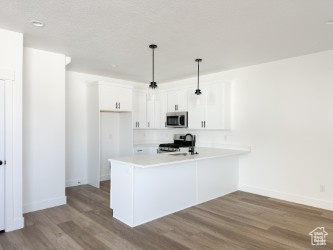 Kitchen featuring stainless steel microwave, dark wood-style floors, a peninsula, range, and white cabinets