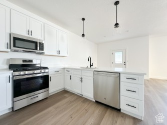 Kitchen featuring appliances with stainless steel finishes, a peninsula, light wood finished floors, and white cabinetry