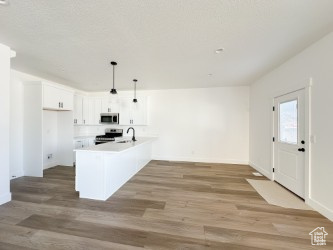 Kitchen featuring stainless steel appliances, light wood-style floors, white cabinets, hanging light fixtures, and light countertops