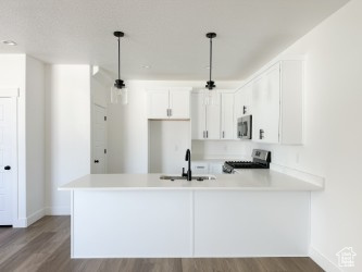 Kitchen with stainless steel microwave, range, wood finished floors, a peninsula, and white cabinets
