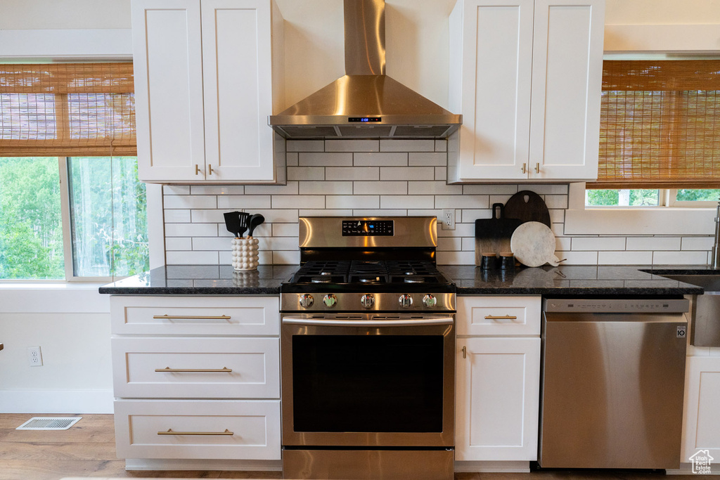 Kitchen featuring wall chimney range hood, appliances with stainless steel finishes, healthy amount of natural light, and decorative backsplash