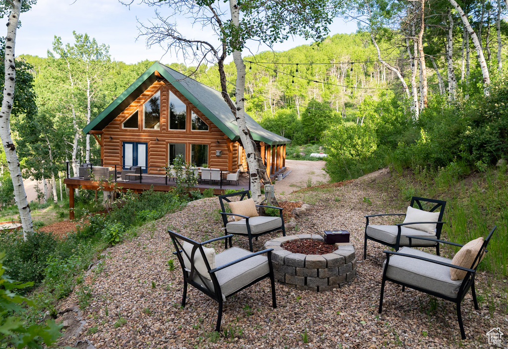 Rear view of property with an outdoor fire pit, a wooden deck, a view of trees, and log siding
