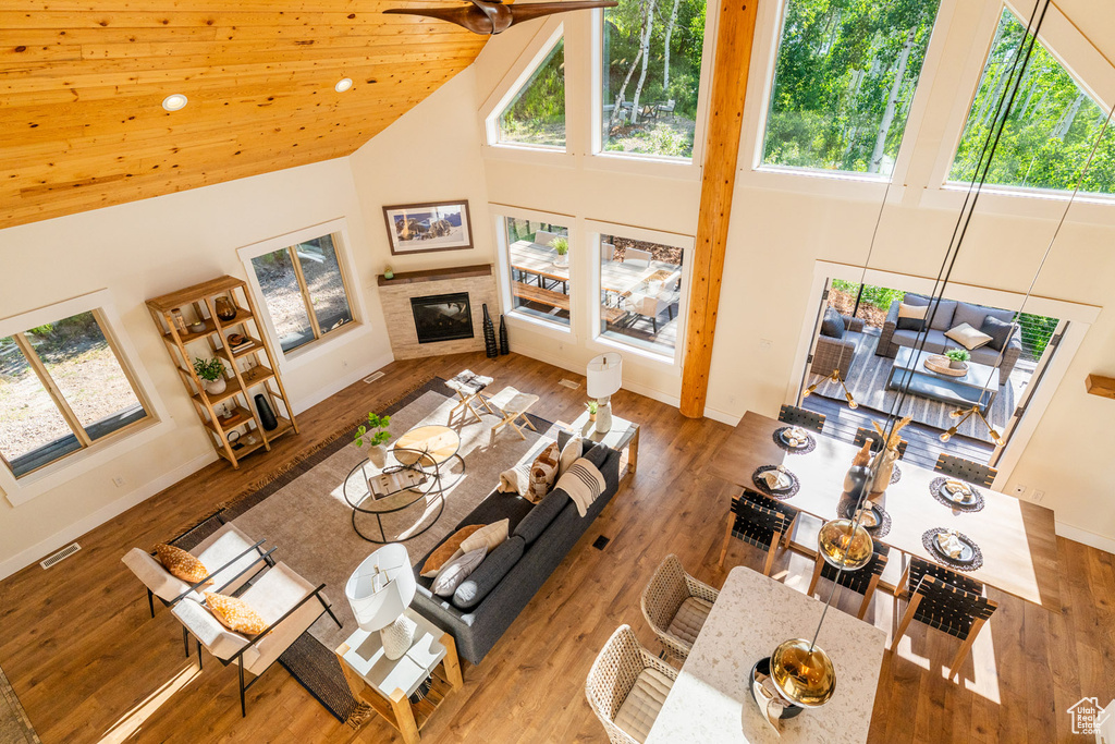 Living room with high vaulted ceiling, healthy amount of natural light, a glass covered fireplace, wood finished floors, and ceiling fan