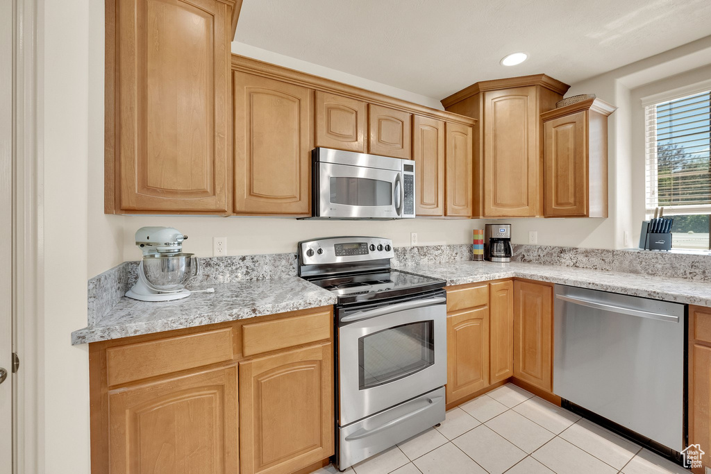 Kitchen with appliances with stainless steel finishes, light tile patterned flooring, light brown cabinetry, recessed lighting, and light stone countertops