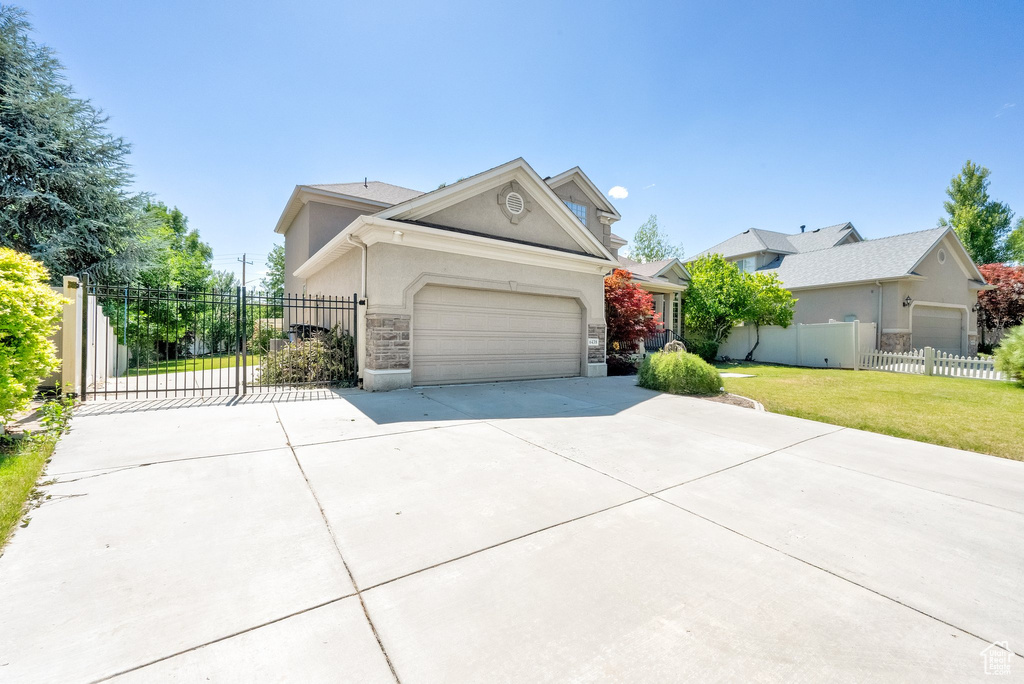 View of front of house featuring driveway, stucco siding, a garage, stone siding, and a gate