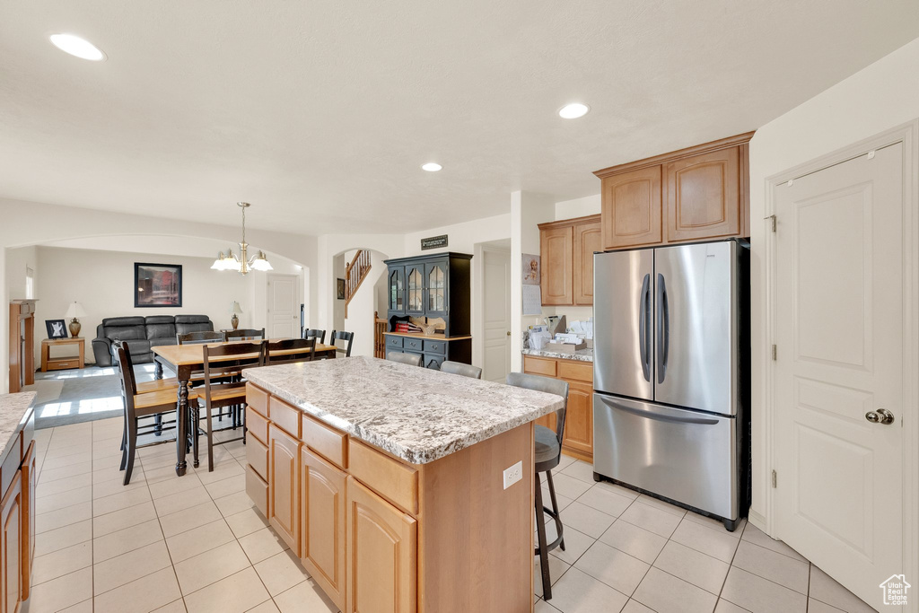 Kitchen with freestanding refrigerator, arched walkways, a center island, a chandelier, and light tile patterned floors