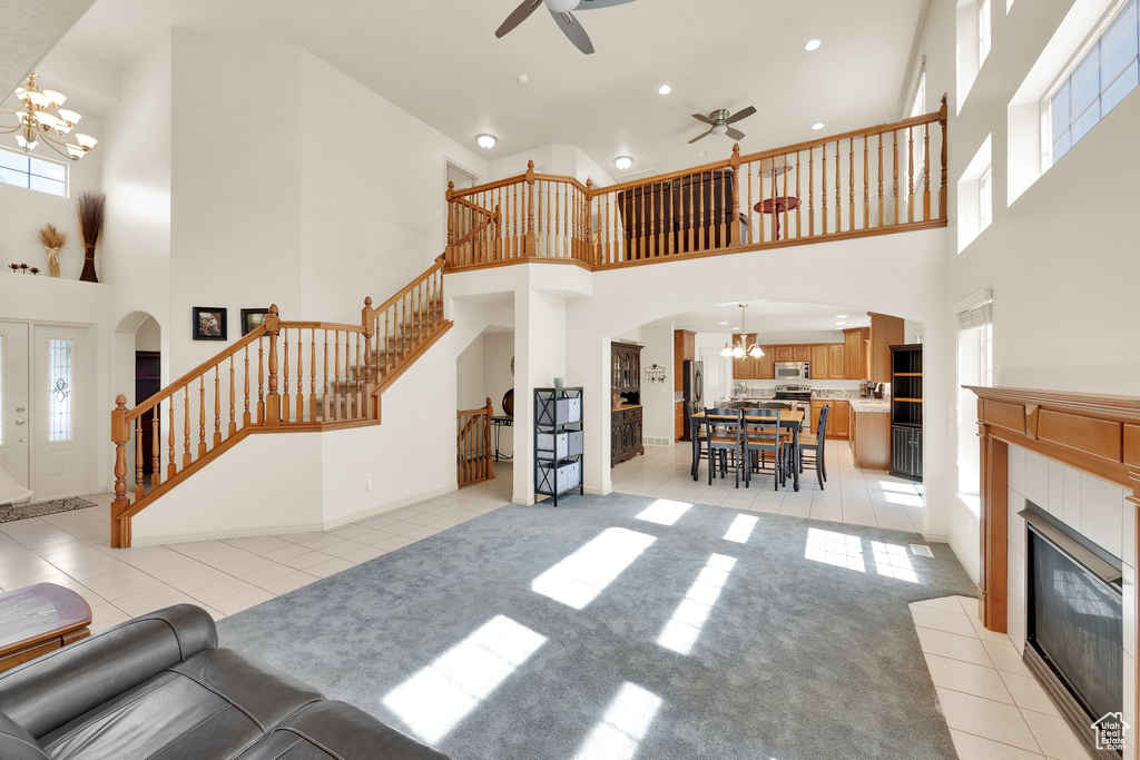 Living room with a ceiling fan, a high ceiling, a chandelier, light tile patterned flooring, and stairway