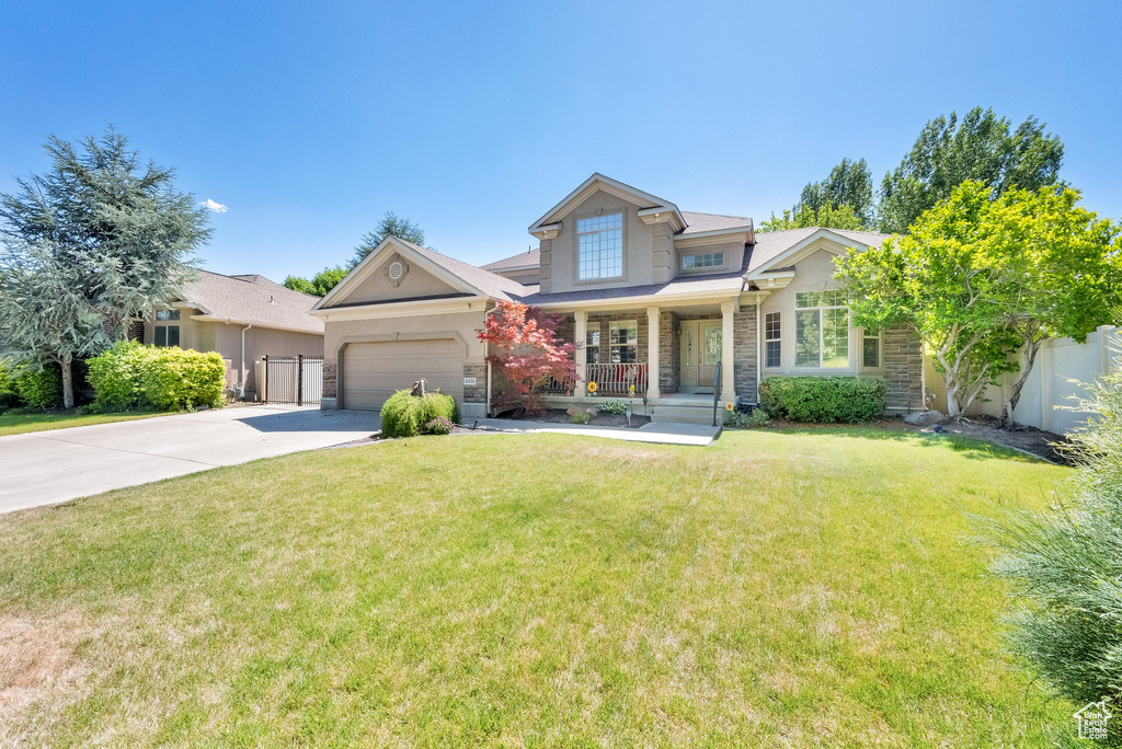 View of front of house with covered porch, concrete driveway, stone siding, a front yard, and a garage