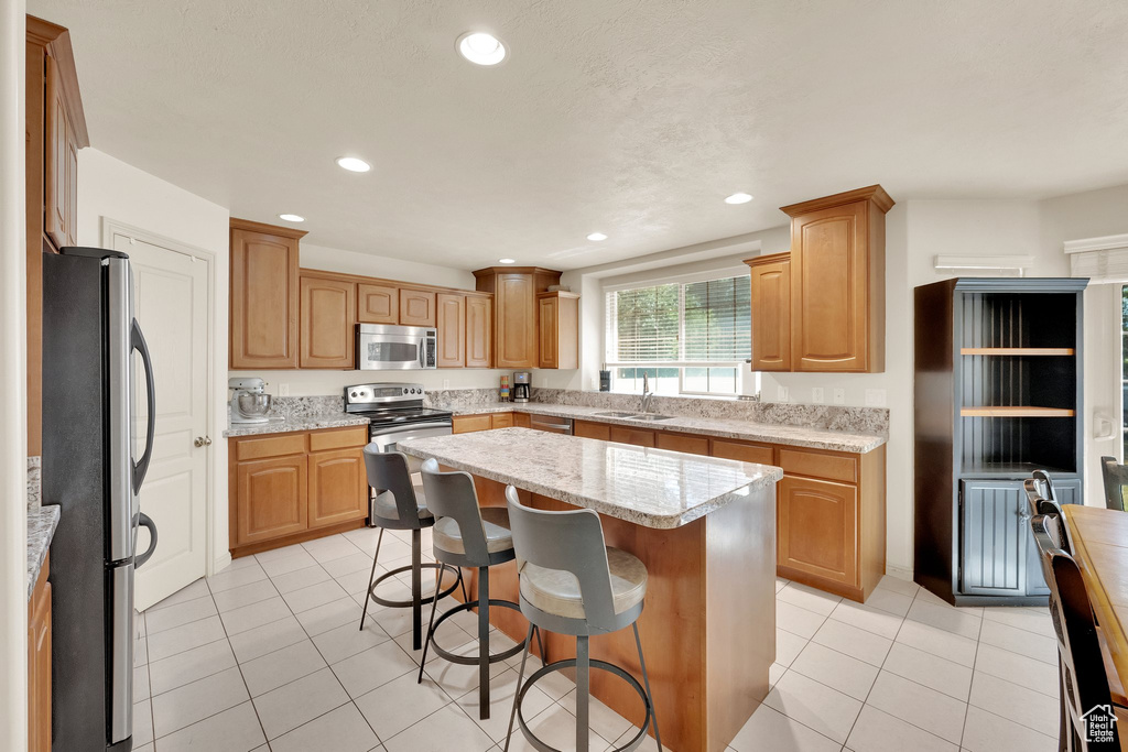 Kitchen featuring stainless steel appliances, a kitchen bar, a kitchen island, recessed lighting, and light tile patterned floors