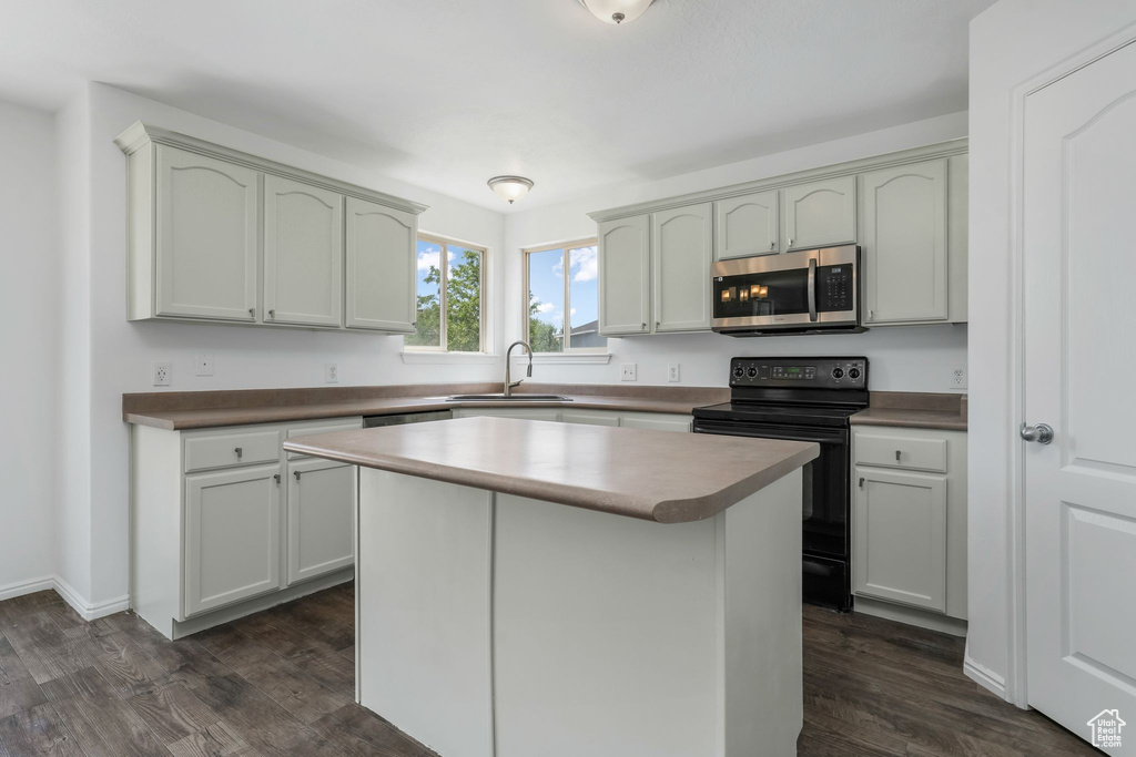Kitchen with stainless steel microwave, electric range, dark wood-style floors, and a center island