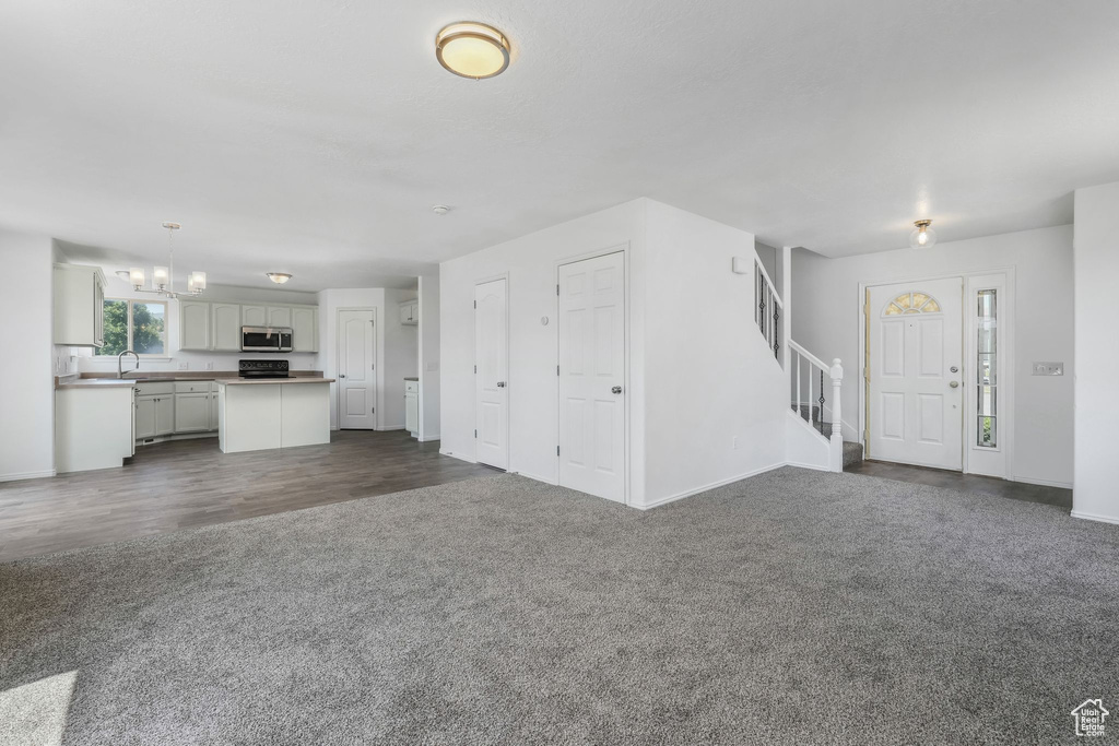 Unfurnished living room with dark carpet, stairs, a chandelier, and dark wood-style flooring