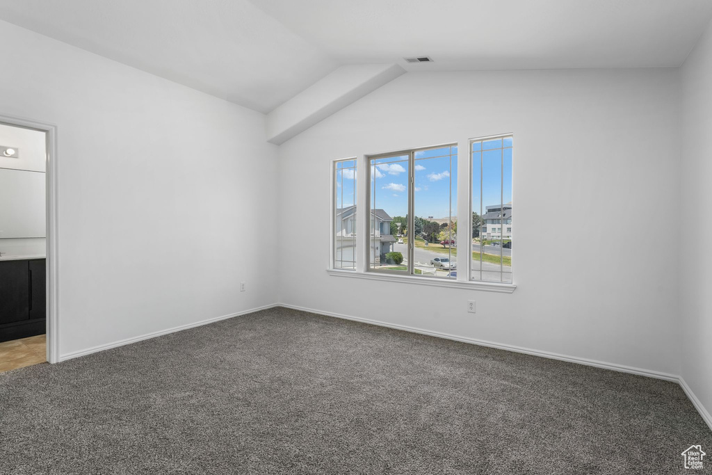 Carpeted spare room featuring lofted ceiling and baseboards