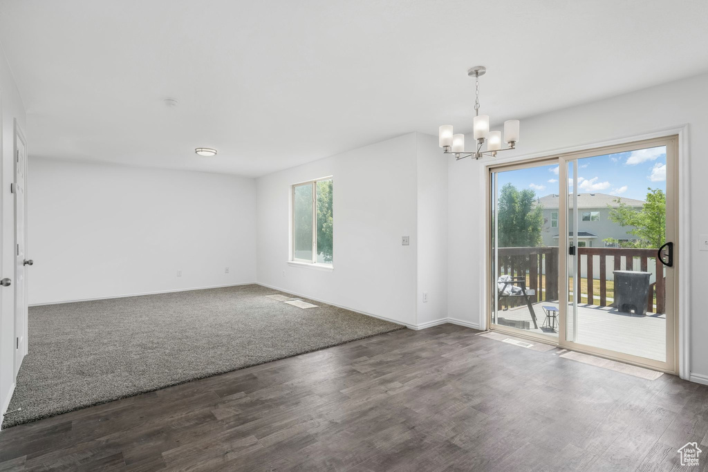 Spare room with healthy amount of natural light, a chandelier, and dark wood-style flooring