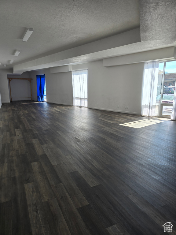 Unfurnished room with dark wood-type flooring, healthy amount of natural light, and a textured ceiling