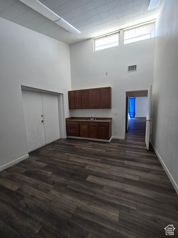 Unfurnished living room featuring a towering ceiling, healthy amount of natural light, and dark wood finished floors