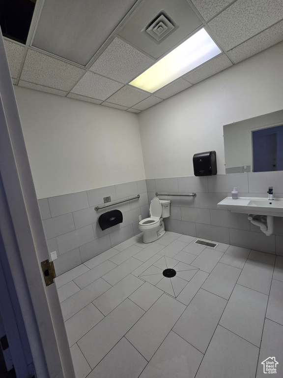 Bathroom with tile walls, a drop ceiling, a wainscoted wall, and tile patterned flooring