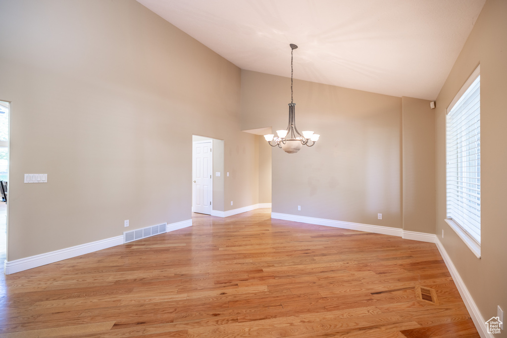 Unfurnished room with a chandelier, plenty of natural light, light wood-style floors, and high vaulted ceiling