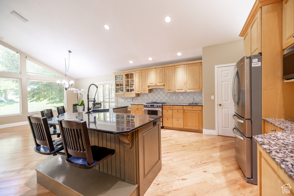 Kitchen featuring appliances with stainless steel finishes, light brown cabinets, backsplash, healthy amount of natural light, and lofted ceiling