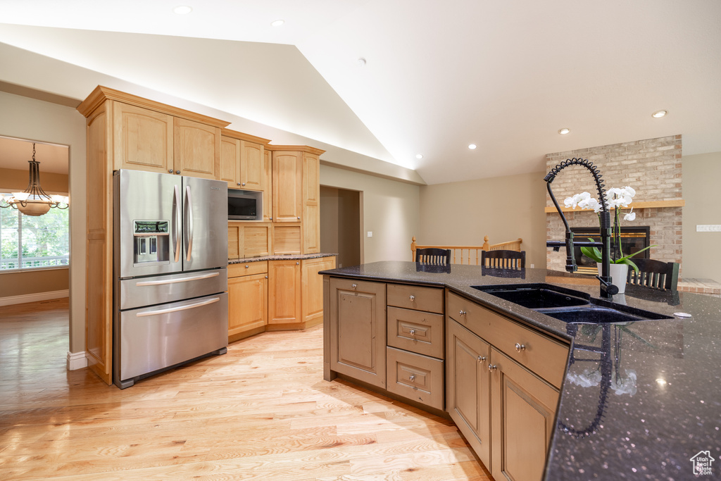Kitchen featuring stainless steel appliances, lofted ceiling, a brick fireplace, light wood-type flooring, and dark stone counters