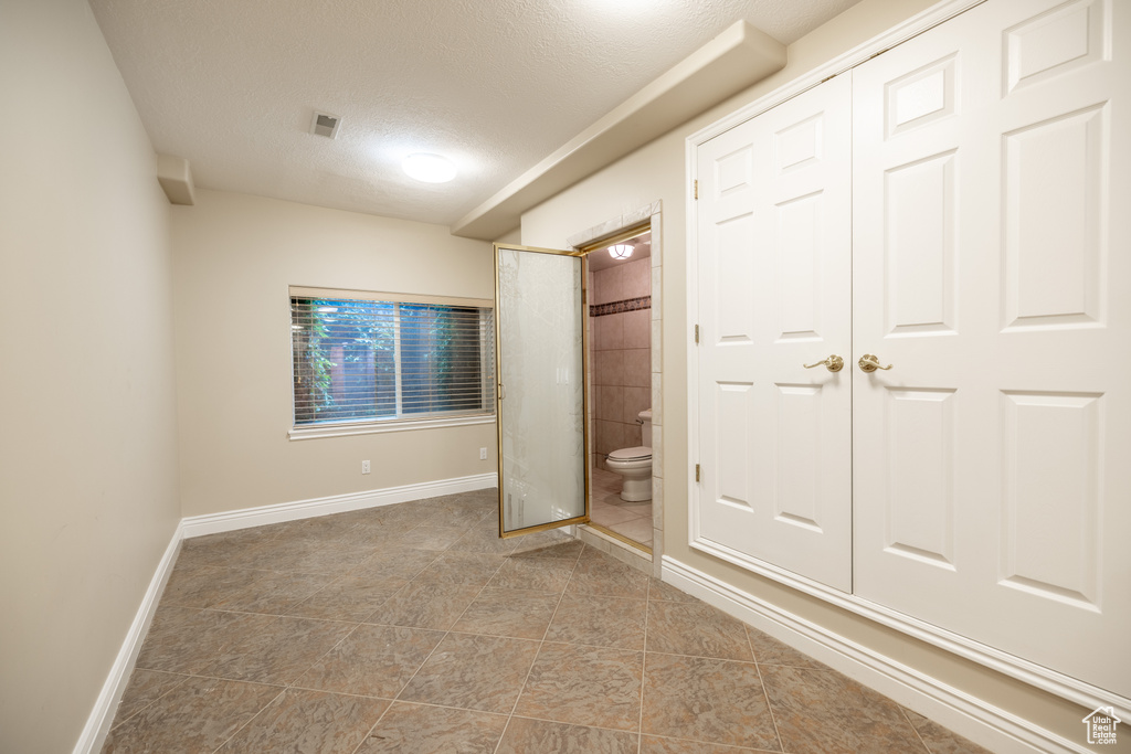 Unfurnished bedroom with a textured ceiling, ensuite bath, and tile patterned floors