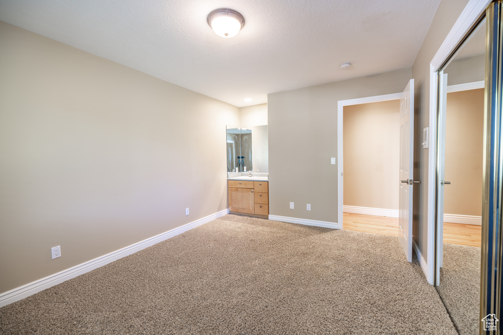Unfurnished bedroom with light colored carpet and connected bathroom