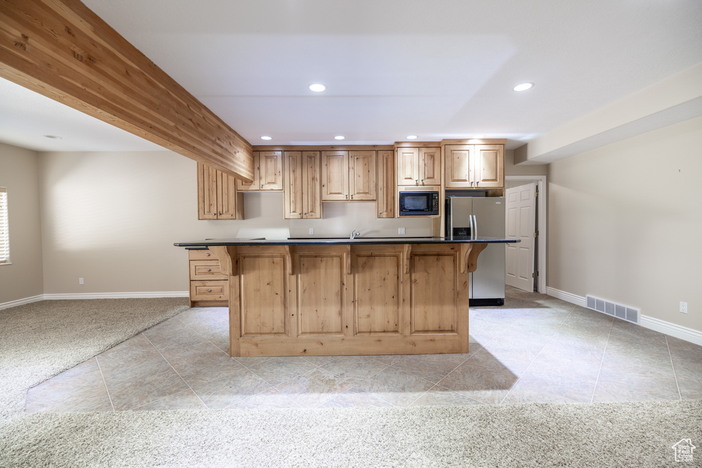 Kitchen featuring black microwave, stainless steel fridge, a breakfast bar, recessed lighting, and light tile patterned flooring
