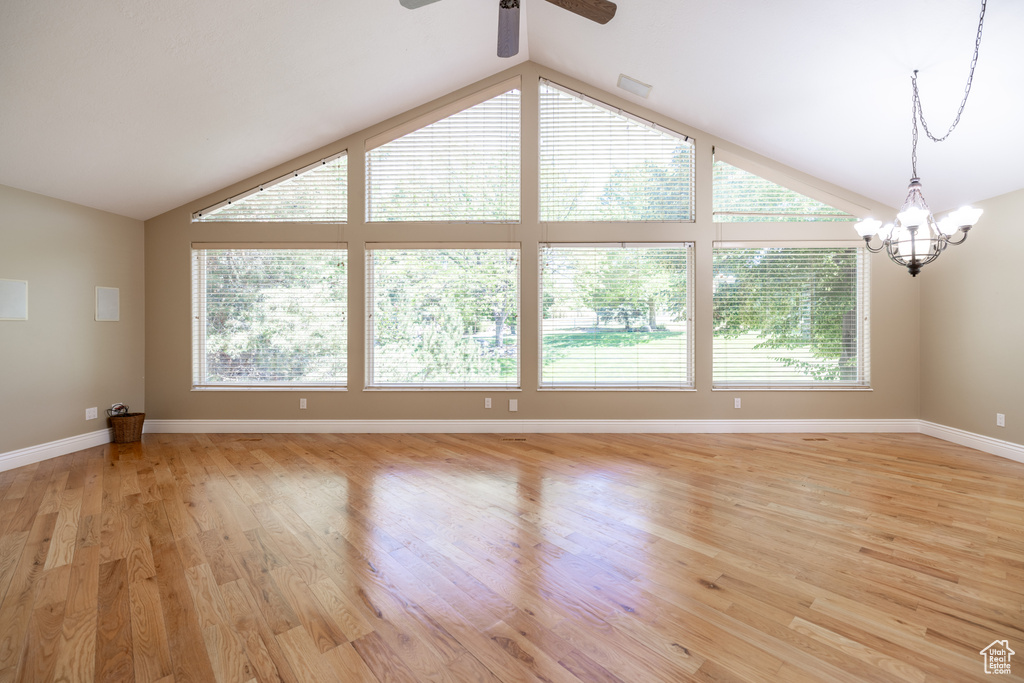 Unfurnished living room featuring lofted ceiling, a ceiling fan, plenty of natural light, a chandelier, and light wood-type flooring